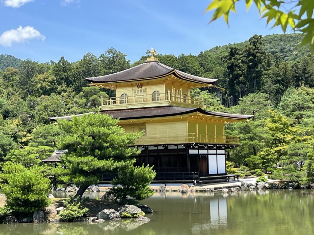 The gold-leaf Kinkaku-ji Golden Pavilion reflecting perfectly on the Mirror Pond under a clear blue sky in Kyoto, Japan.