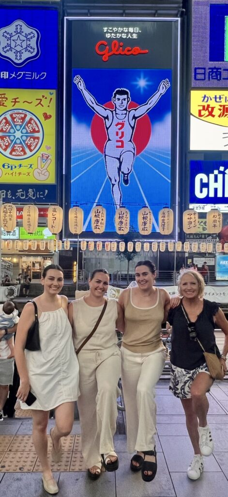 Mother and adult daughters in front of the famous Glico Running Man sign in Dotonbori Osaka Japan at night