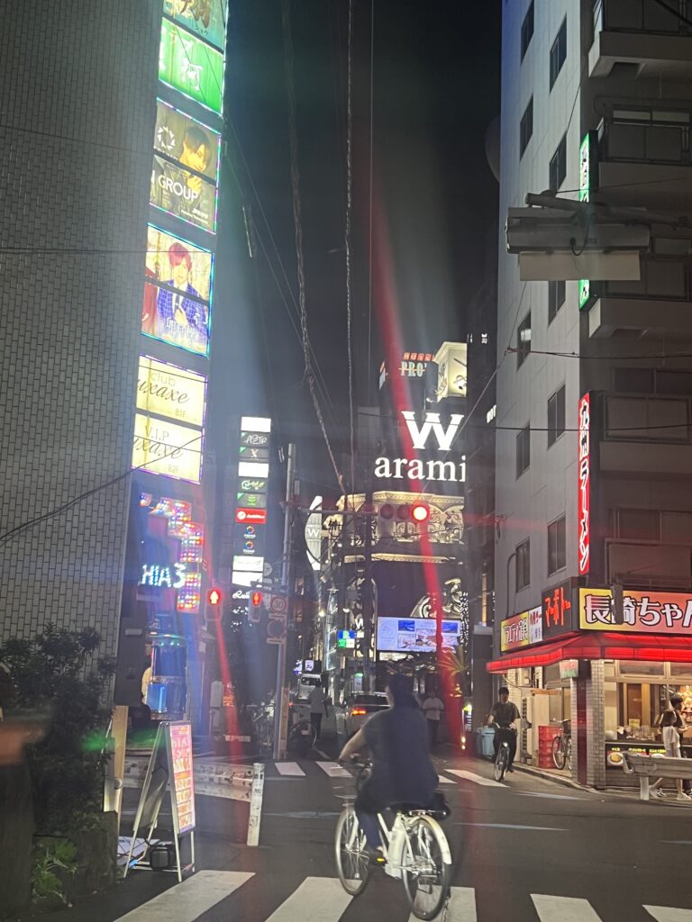 Nighttime street scene in Shinjuku, Tokyo with neon signs, restaurants, and cyclists near Hotel Century Southern Tower